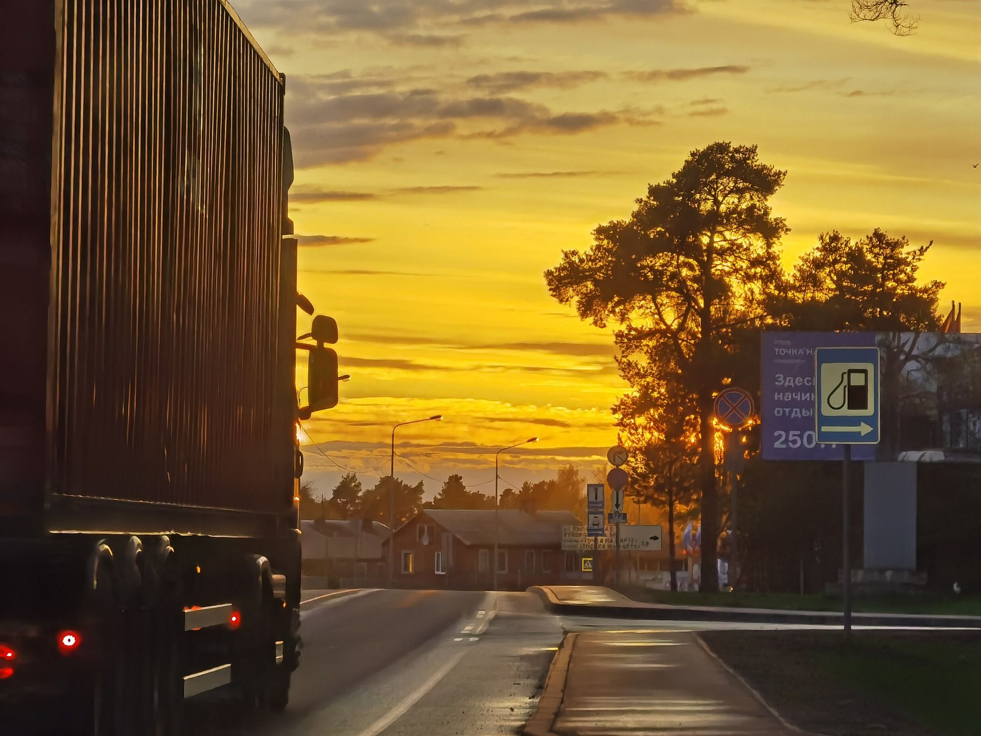 Trailer on a wet road at sunset, passing a fuel station sign